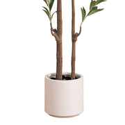 An artificial potted plant with two brown faux tree trunks, green leaves, and a matte off-white cylindrical pot, isolated on a white background.