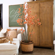 Decorative plant in a woven basket on a coffee table with a wooden cabinet and framed artwork in the background.