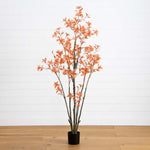Potted artificial plant with orange leaves on a wooden floor against a white wall