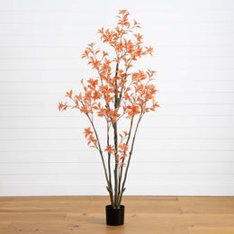 Potted artificial plant with orange leaves on a wooden floor against a white wall
