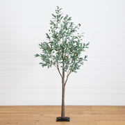 An artificial eucalyptus tree with green leaves and brown branches, standing on a black rectangular base against a white shiplap wall and light wood floor.