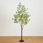 An artificial eucalyptus tree with green leaves and warm white string lights, standing on a black base against a white shiplap wall and light wood floor.