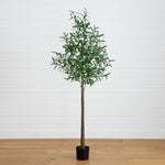 A tall artificial olive tree with green leaves and a brown trunk, potted in a black plastic container, set against a white shiplap wall and light wood floor.