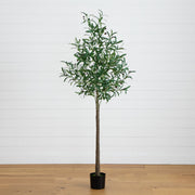A tall artificial olive tree with green leaves and a brown trunk, potted in a black plastic container, set against a white shiplap wall and light wood floor.