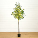 An artificial olive tree with green and yellow variegated leaves, a brown trunk, and a black pot, standing on a light wood floor against a white shiplap wall.