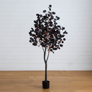 Artificial tree with black and red leaves on a wooden floor against a white wall.