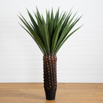 Tall artificial plant with decorative pot on a wooden floor against a white wall