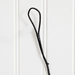 A single black leather or faux-leather loop hook hanging against a white paneled wall.