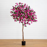 An artificial bougainvillea tree with bright pink flowers and green leaves, mounted on a brown trunk in a black pot, set against a white paneled wall and light wood floor.