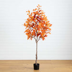 Artificial orange tree in a pot on a wooden floor with a white wall background