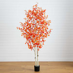 Artificial potted tree with orange leaves on a wooden floor against a white wall