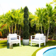 Two white chairs with cushions on a grassy area near a pool, surrounded by palm trees.