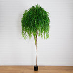 Artificial potted plant with green leaves on a wooden floor against a white wall.
