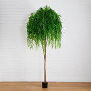 Artificial potted plant with green leaves on a wooden floor against a white wall.