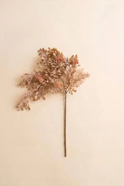 A single dried decorative branch with clustered small leaves in warm beige, tan, and muted rust tones, attached to a long brown stem against a plain cream background.