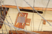 Model ship with a grater on the deck, viewed through chain-link fence.