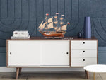 Wooden sideboard with decorative ship model against a blue wall