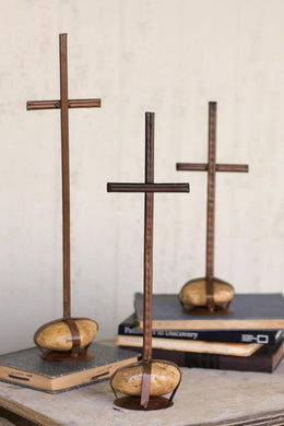 A set of three rustic brown metal crosses with caged rock bases, displayed on a flat surface.
