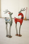 A set of two recycled red iron deer figurines with painted finishes standing on a floor.